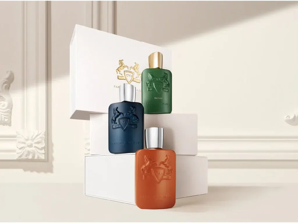 Три флакони Parfums de Marly на білих подарункових коробках у світлому інтер'єрі з декоративними панелями