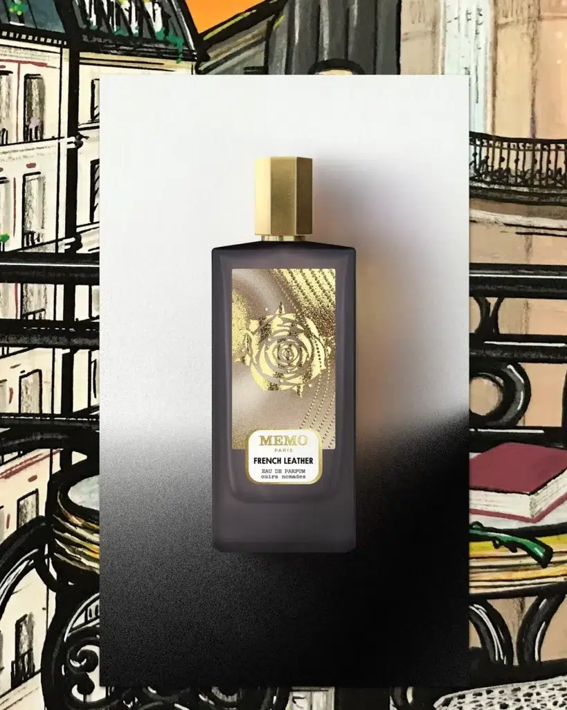 Темний флакон Memo French Leather із золотою кришкою на тлі намальованого паризького балкона з кавовим столиком