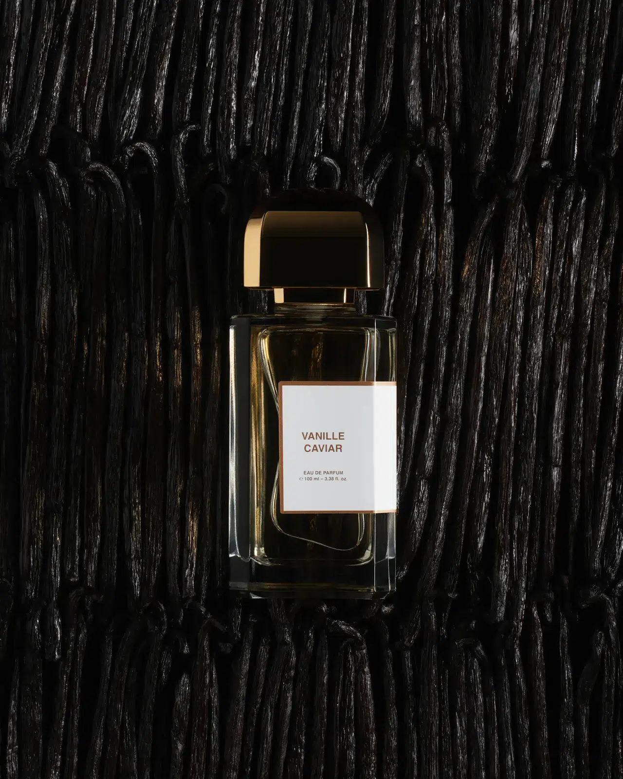 Флакон BDK Parfums Vanille Caviar із золотою кришкою на тлі щільних рядів темних стручків ванілі