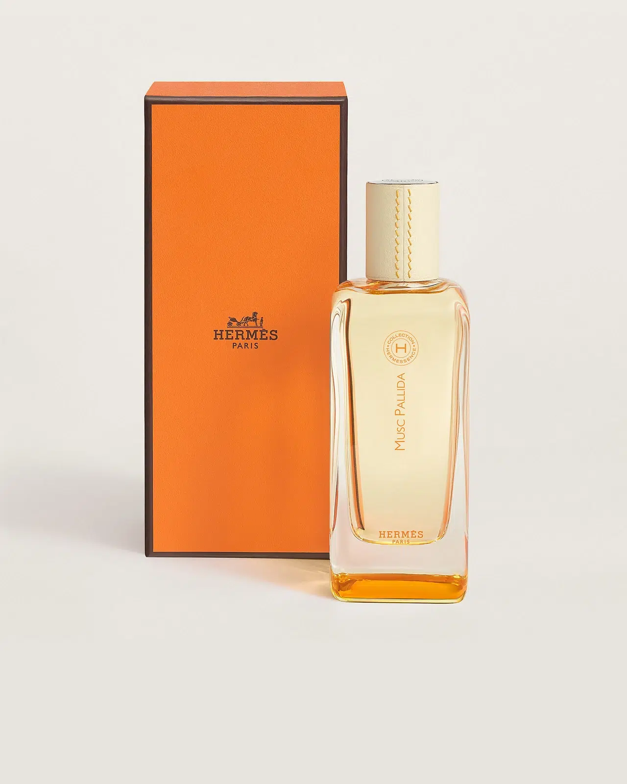 Флакон Hermès Musc Pallida з кремовою шкіряною кришкою поруч із помаранчевою коробкою Hermès на світлому тлі