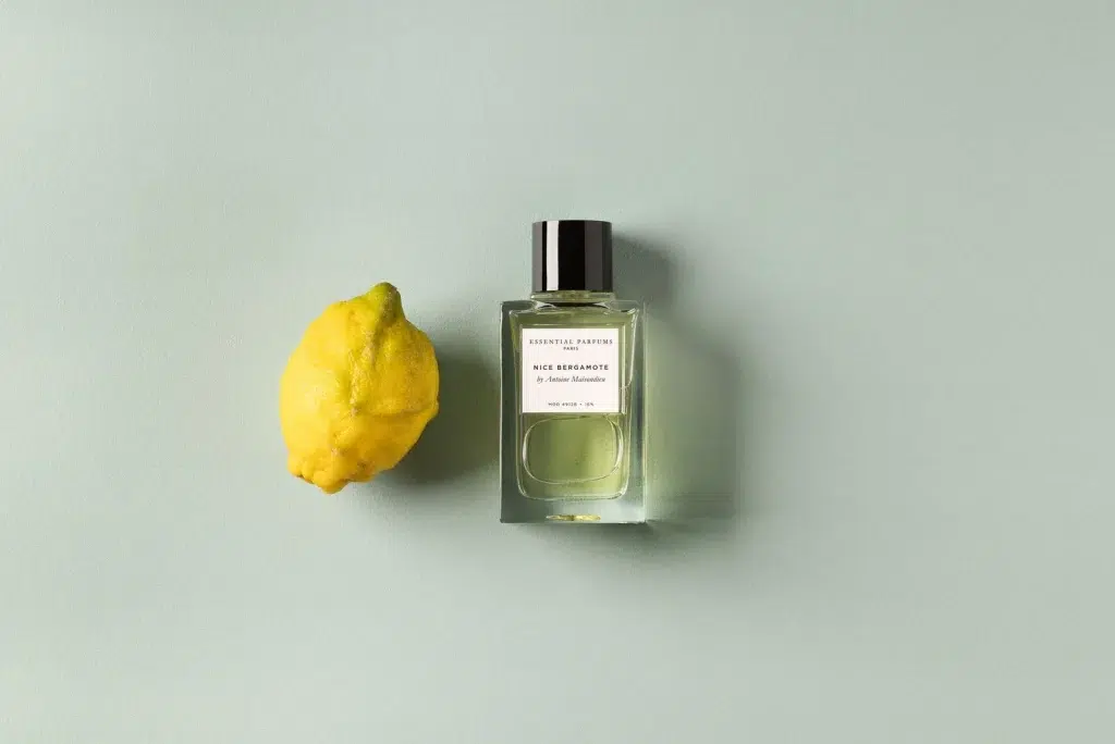 Флакон Essential Parfums Nice Bergamote з чорною кришкою поряд із жовтим цитрусом на світло-зеленому тлі